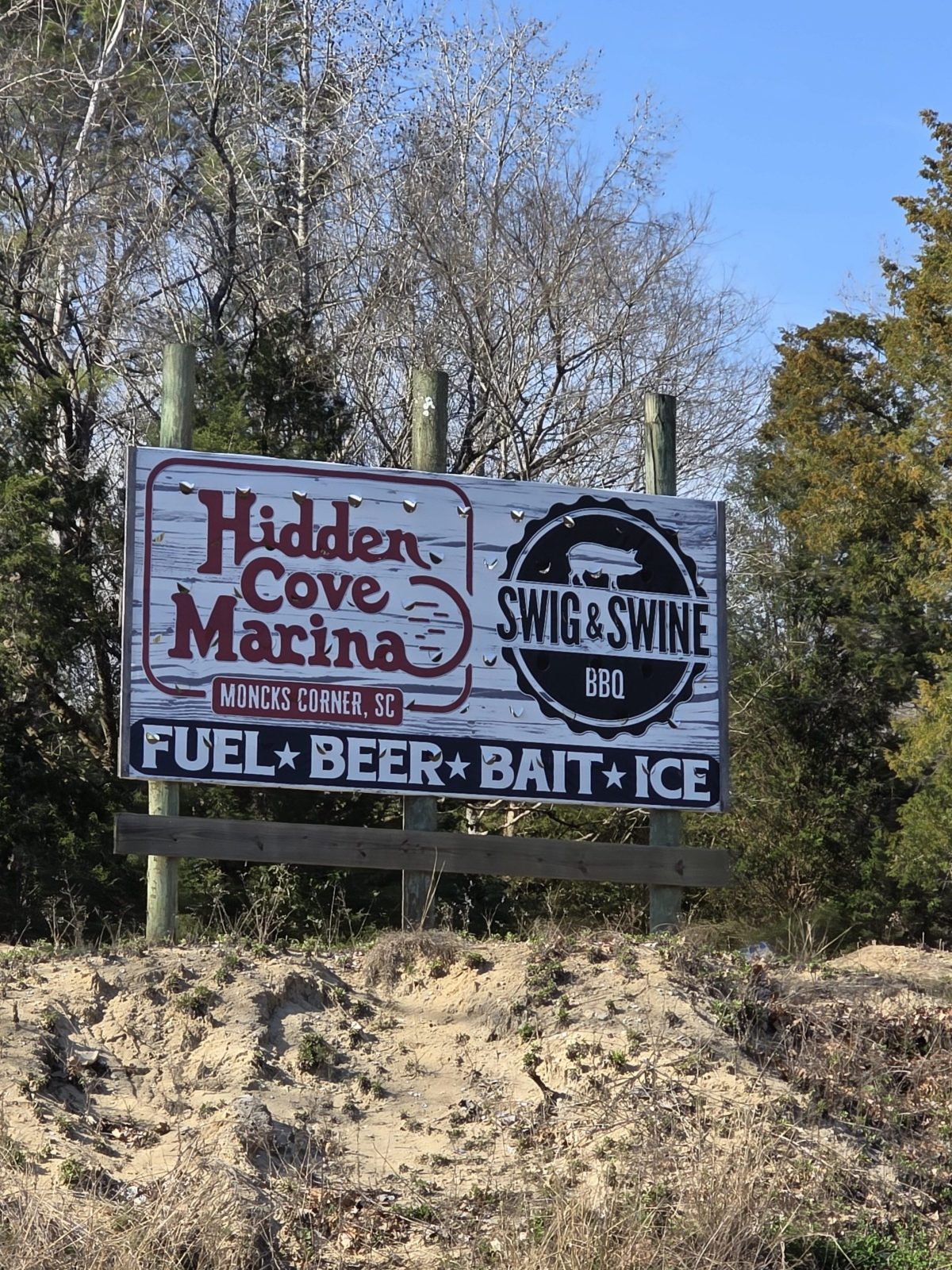 Sign for Hidden Cove Marina and Swig & Swine BBQ on a sandy hill with trees in the background.