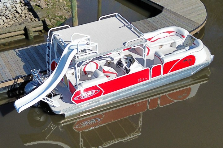 A red and white pontoon boat with a slide docked on calm water.