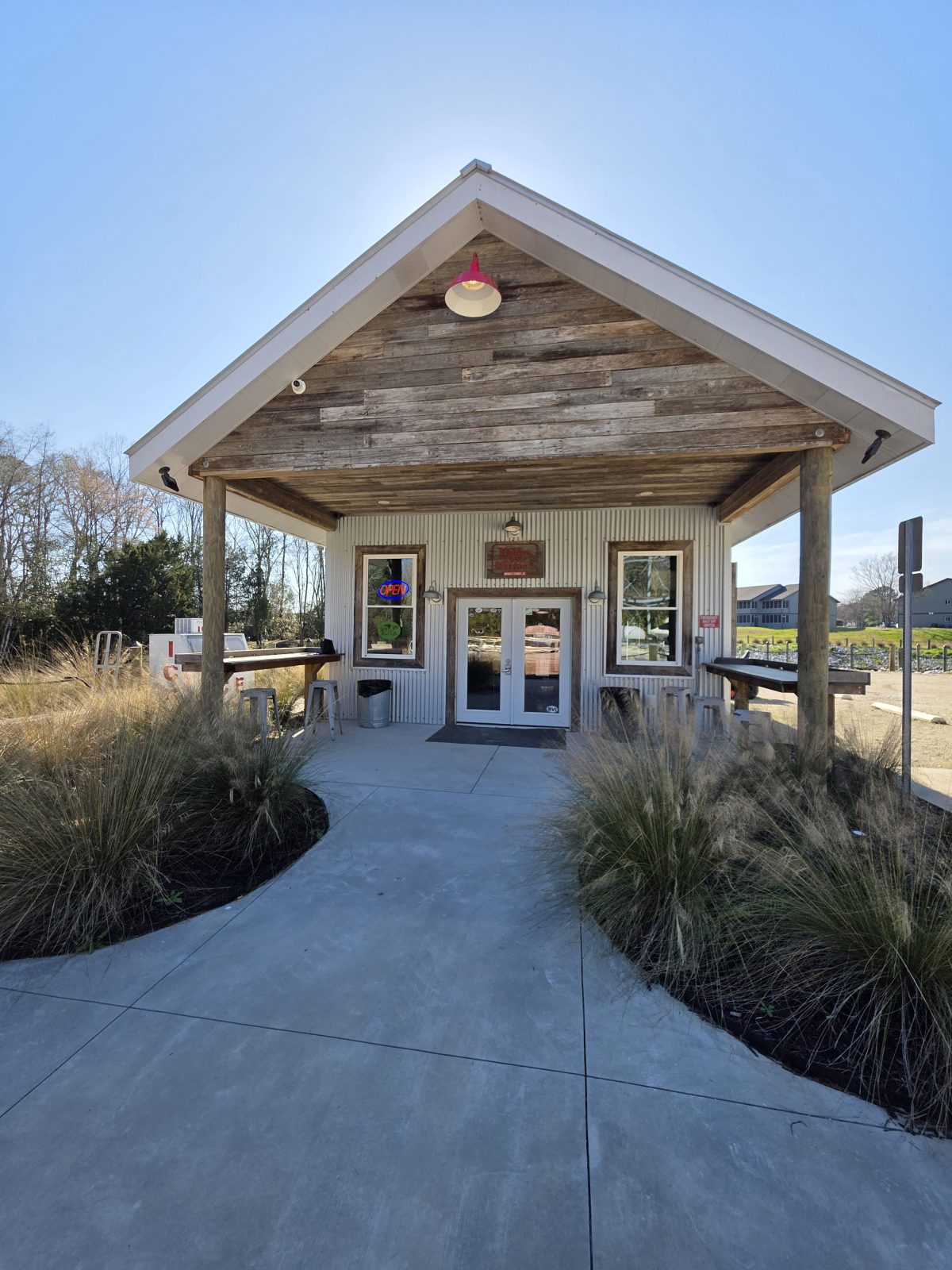 Small rustic cafe with wooden exterior and open sign, surrounded by grass on a clear day.