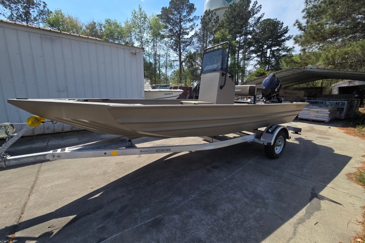 Aluminum boat on trailer in a yard with trees and a water tower in the background.